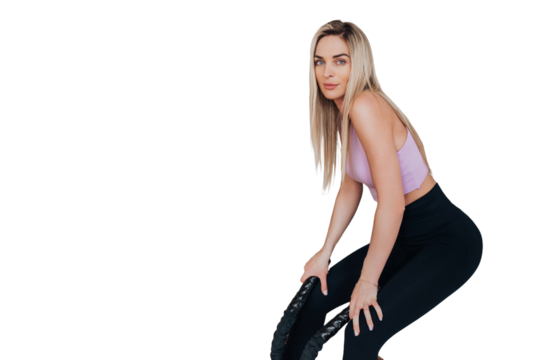 Tired young American young woman in sportswear leans on wall holds battle ropes resting after workout against transparent background. Weight loss exercise, healthy people. Fit girl at break