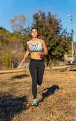 Beautiful young runner girl, dressed in tight sportswear and white top, illuminated in the face by dawn sunlight, running happy and free through a mountain park leaving her shadow behind.