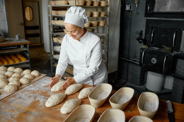 Professional positive woman baker forming loaf from raw dough - obrazy, fototapety, plakaty