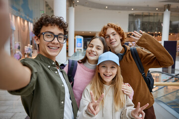 Happy teenage friends taking selfie by phone camera at shopping mall