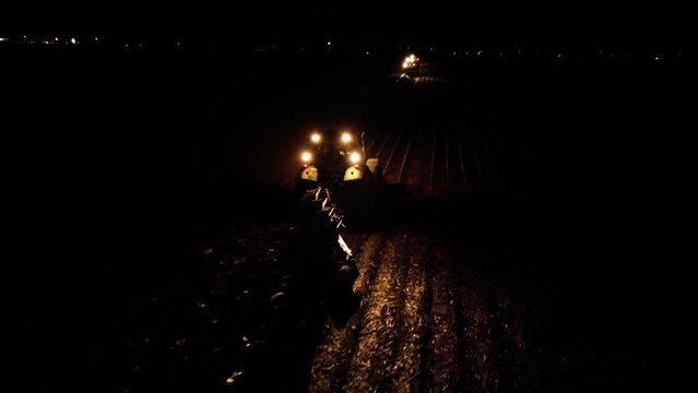 High angle drone shot of tractors plowing at night. Evening farming. Industrial machinery tilling agricultural land in the dark. Plough  running through soil. Aerial footage of growing food.
