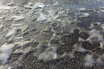 Calm sunny spring day with melting snow and ice on the asphalt surface