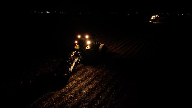 High angle drone shot of tractors plowing at night. Evening farming. Industrial machinery tilling agricultural land in the dark. Plough  running through soil. Aerial footage of growing food.
