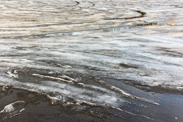 Spring warming, melting snow and ice on black asphalt