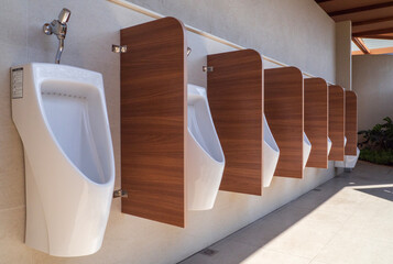 modern clean public restroom with tiles. Line of men's white urinals in public restrooms.