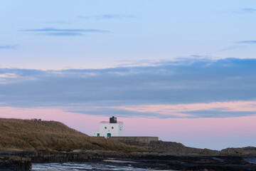 Beautiful landscape image of Northumberland beach in Northern England during Winter dawn with deep orange sky