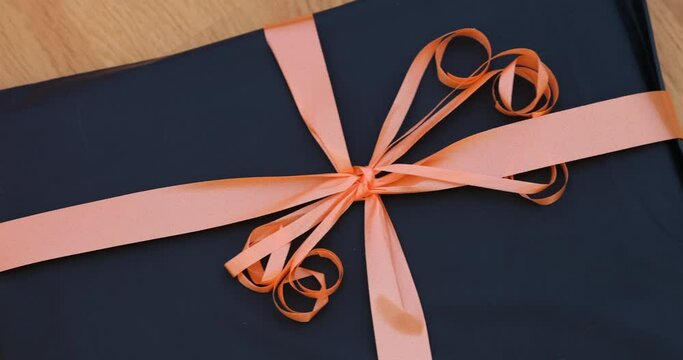 A black gift with an orange bow on a wooden background.