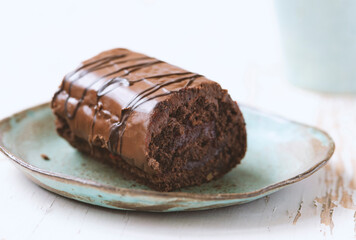 Chocolate roll cake in plate on white wooden background.
