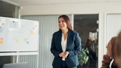 CEO laughing while giving a whiteboard presentation to businesspeople in an office