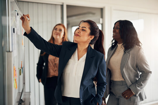 Smiling businesswoman and her team brainstorming together on an office whiteboard
