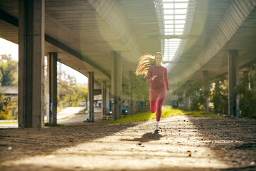 A sporty runner running towards camera under the bridge.
