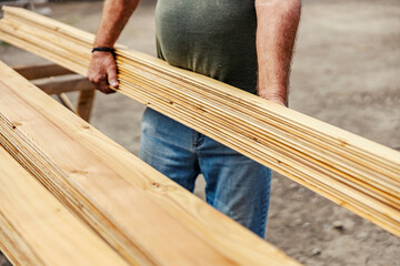 Cropped picture of worker's hands carrying wooden material on site.