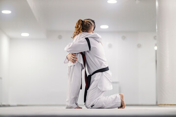 A little girl is hugging her trainer on Taekwondo class in martial art school.