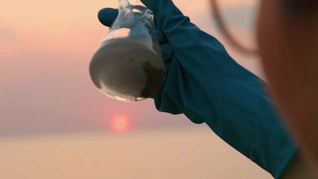 Close up view of hand in rubber glove testing sample flask of dirty water. Concept of pollution and ecology
