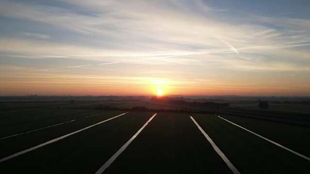 sun rises on arable farmland in green heart of Netherlands near Woerden. Drone photography picks up reflection in field drainage sluits