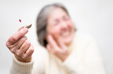 An unrecognizable elderly woman shows the camera a BTE hearing aid while pointing to her ear...