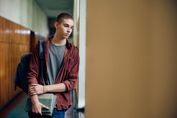 Thoughtful student standing alone in high school hallway.