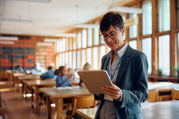Happy high school teacher using digital tablet in classroom.