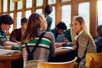 Happy high school student talks to her friend during class in library.