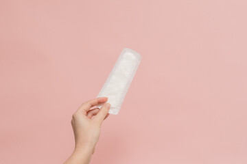 Woman's hand holding sanitary pad on pink background © Antonio