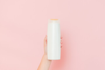 Hands holding shampoo, hair conditioner or body lotion bottle in pink background. Cosmetics bottle
