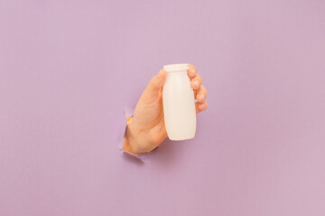 White bottle of probiotic yogurt for digestive system in hand with lilac background. Dietary...