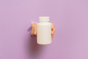 Cool view on white bottle plastic tube in hands on lilac background. Packaging for pills, capsules or supplements. Cosmetics