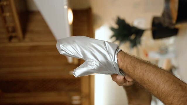 A person's arm wearing a silver oven mitt, presumably to handle hot items, with a blurred kitchen background. This image is ideal for stock videos demonstrating kitchen safety and equipment.