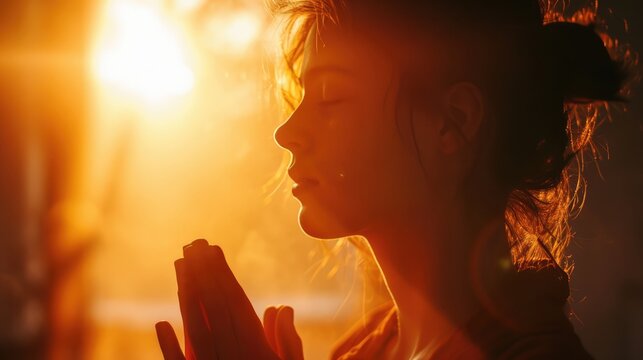 Young woman praying on the background of the setting sun.