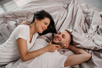 Fototapeta na wymiar Loving woman gently touching man's face as they smile and enjoy a tender moment, lying in a cozy bed with soft lighting