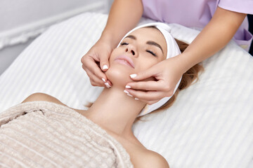 Fototapeta na wymiar Beautiful woman receiving facial massage in beauty salon. Skin care.