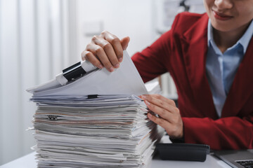 Close up hands of person in a red blazer organizing a substantial stack of various papers, likely...