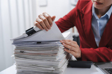 Close up hands of person in a red blazer organizing a substantial stack of various papers, likely...