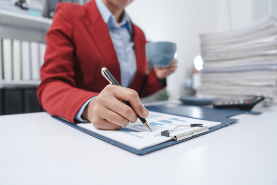 individual in a red blazer, analyzing a bar graph on a clipboard while holding a coffee mug, indicative of working on yearly tax documents.