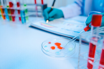 Asian people scientist in lab coat and protective gloves working with test tubes with green and red liquids, with microscope and other test tubes in the background in laboratory.