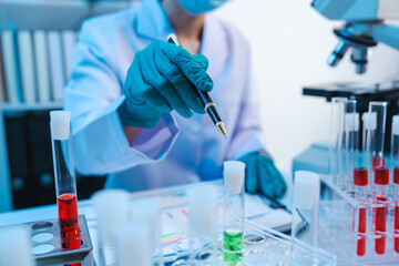 Asian people scientist in lab coat and protective gloves working with test tubes with green and red...