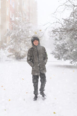 A boy walks along a snowy street, it is snowing, blizzard and frost on a winter day