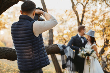 Professional male wedding photographer taking pictures of the bride and groom in nature in autumn