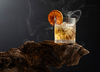 Smoked old fashioned cocktail with ice and dried orange slice.