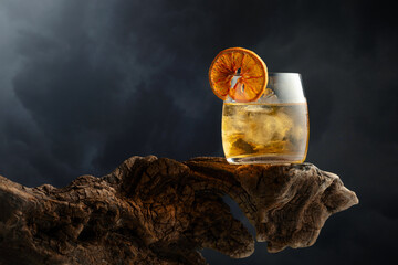 Old fashioned cocktail with ice and dried orange slice on a old snag.