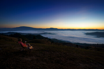Fototapeta na wymiar Pretty Asian Woman is happy with the beautiful scenery of the sea of mist in the morning at the Car Camping site with a viewpoint of is fresh nature of the top of Mountain Chiang Mai, Thailand.