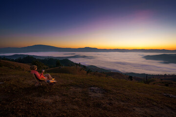 Pretty Asian Woman is happy with the beautiful scenery of the sea of mist in the morning at the Car Camping site with a viewpoint of is fresh nature of the top of Mountain Chiang Mai, Thailand.