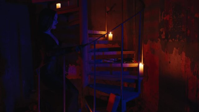 A gothic sexy woman coming up the old stairs and picking up a red rose in slow motion, wearing a black halloween dress and gloves. Indoors, nighttime. Slow motion