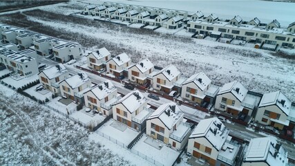 Aerial view of rows of identical houses covered in snow, with solar panels also covered by white snow on the roofs, on a cold and freezing day.