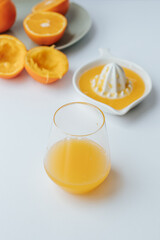 on a white background there is a glass glass with orange juice, next to it there is a manual juicer and a plate with squeezed oranges
