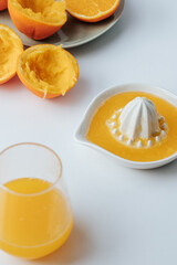 on a white background there is a glass glass with orange juice, next to it there is a manual juicer and a plate with squeezed oranges