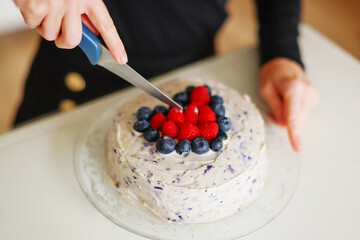 female hands of the pastry chef cut cream pie with blueberries and raspberries on a table