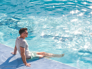 Handsome man sitting near the swimming pool of a cruise ship. Sunny morning, clear day. View from...