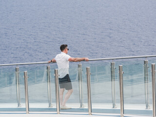 Handsome man standing on the empty deck of a cruise liner against the backdrop of sea waves. Sunny, clear day. Closeup, outdoor. Vacation and travel concept