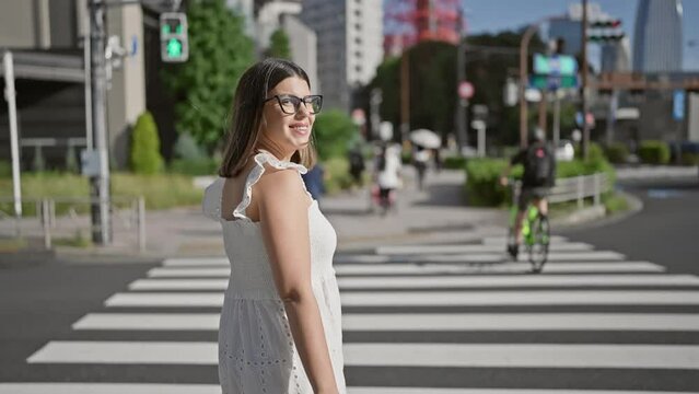 Beautiful hispanic woman in glasses, smiling and looking back at camera, walking across tokyo street crosswalk